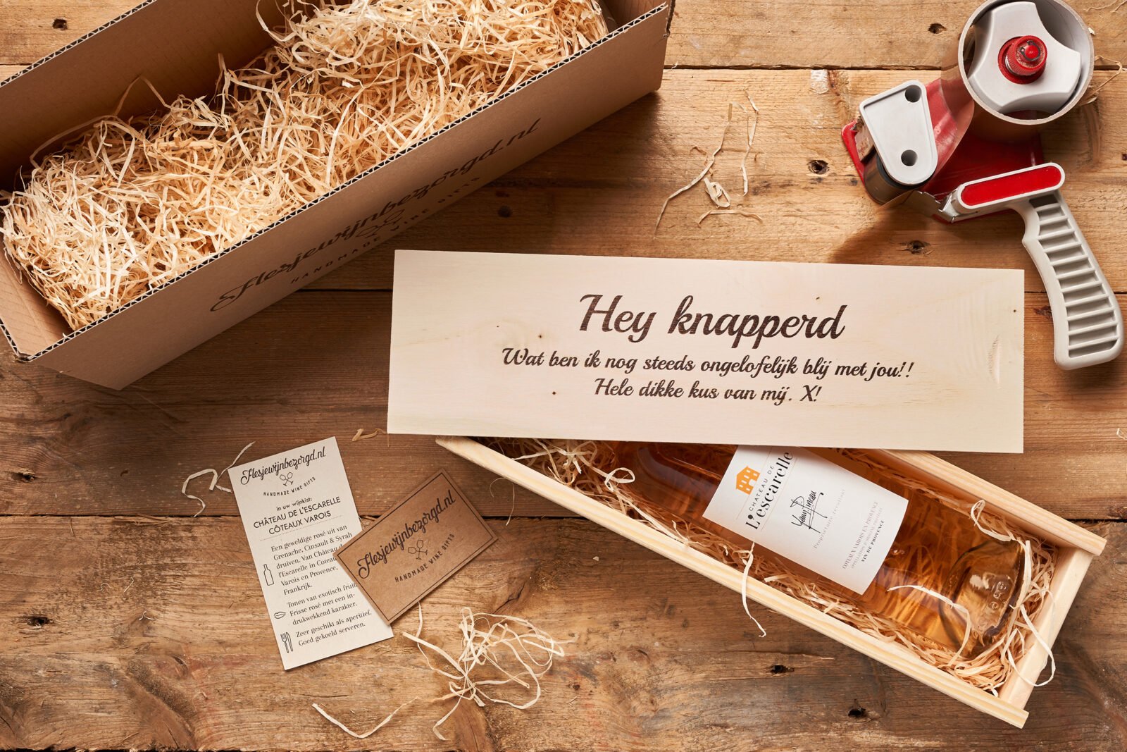 Fles rosé in wijnkist op tafel met bedrukte deksel ernaast.